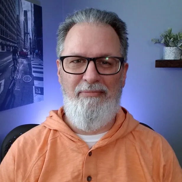 Darren, smiling, with glasses and a grey beard, in an orange hoodie